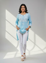 model is wearing and posing in this sky blue colour short length Chikankari kurti with white floral hand embroidery with white jeans
