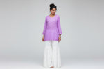 model is wearing purple short chikankari embriodery kurti with white hand embrioderd flared trousers in queens garden in london 