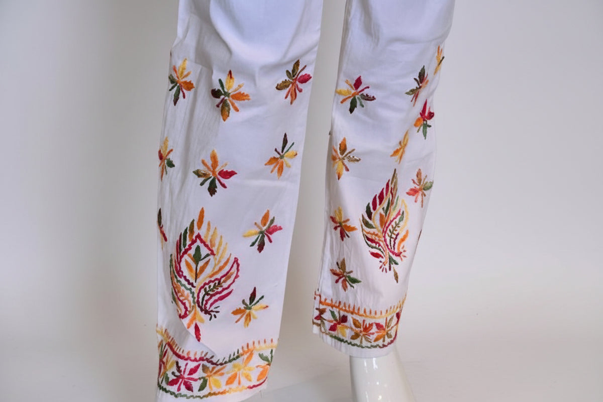 A pair of white stretchable cotton pants with pockets both sides and multicolour thread floral embroidery, featuring a relaxed fit with an adjustable drawstring waistband.