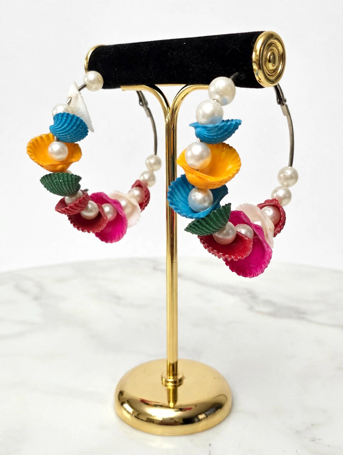 Multicolour shell-shaped hoop earrings with faux pearls on a gold-tone display stand