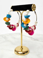 Multicolour shell-shaped hoop earrings with faux pearls on a gold-tone display stand