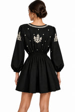 The rear view of a black long-sleeve dress with white floral embroidery and small white bead details