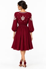 The rear view of a maroon three-quarter sleeve dress with white embroidered patterns on the bodice and sleeves.