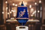 Blue embroidered garment on a mannequin with a blurred background of lights