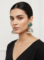 Pair of ornate silver and green stone earrings on a display stand.