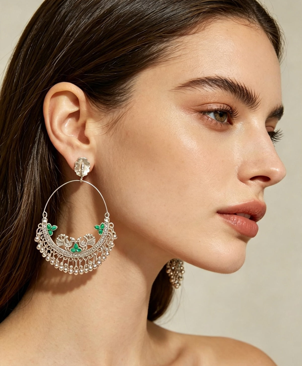 Model wearing oxidized silver peacock chandbali hoop earrings with emerald green stone accents and ghungroo fringe — antique silver finish, premium ethnic jewelry by Famaza Couture.