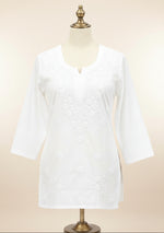 A bright pink tunic top with floral embroidery on the front, displayed on a cream dress form with a gold-colored stand against a white background.