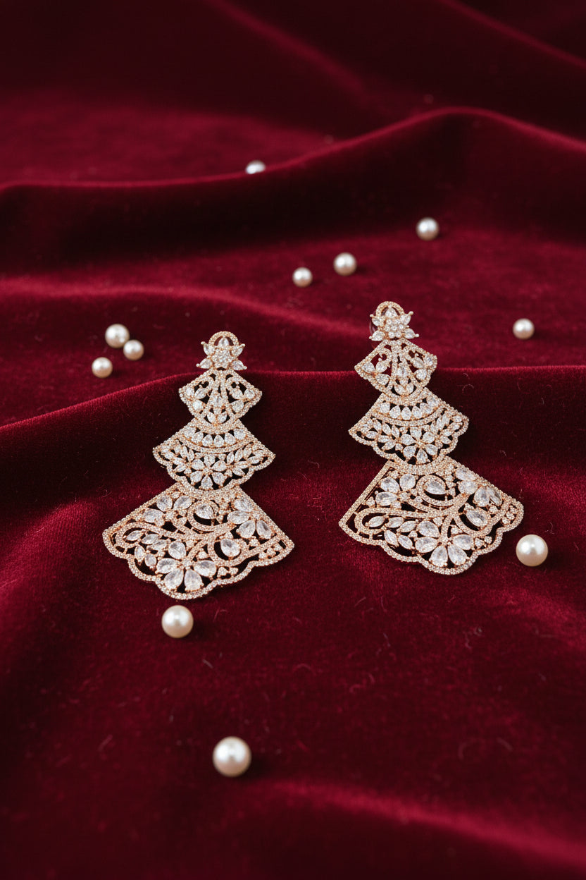 pair of Rose gold-tone three-tiered chandelier earrings with intricate filigree lattice metalwork and sparkling cubic zirconia crystals, displayed on a red velvet jewellery bust.