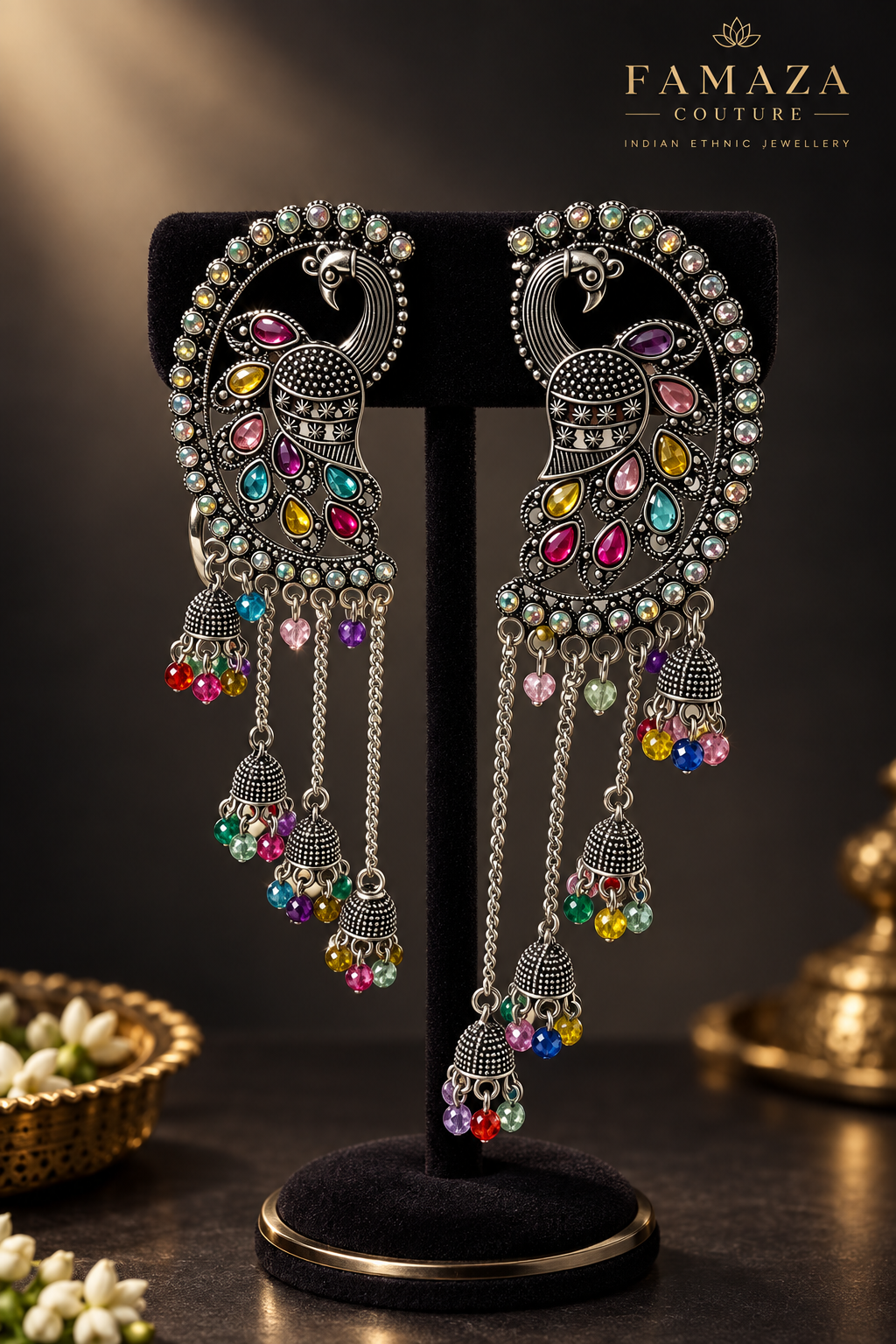 Antique silver peacock meenakari chandbali jhumka earrings with vibrant multicolor gemstone detailing and long chain tassel drops, displayed on elegant black velvet stand — Indian Pakistani bridal ethnic jewelry.