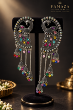 Antique silver peacock meenakari chandbali jhumka earrings with vibrant multicolor gemstone detailing and long chain tassel drops, displayed on elegant black velvet stand — Indian Pakistani bridal ethnic jewelry.