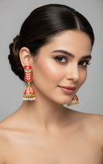 red colour pair of gold-platedMeenakari drop Jhumka earrings displayed on a stand, featuring intricate designs and studded with stones.