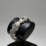 Famaza Couture Silver Crystal & White Pearl Luxury Bangle Bracelet — displayed on sleek black jewelry stand, showcasing pave crystals and white pearls.