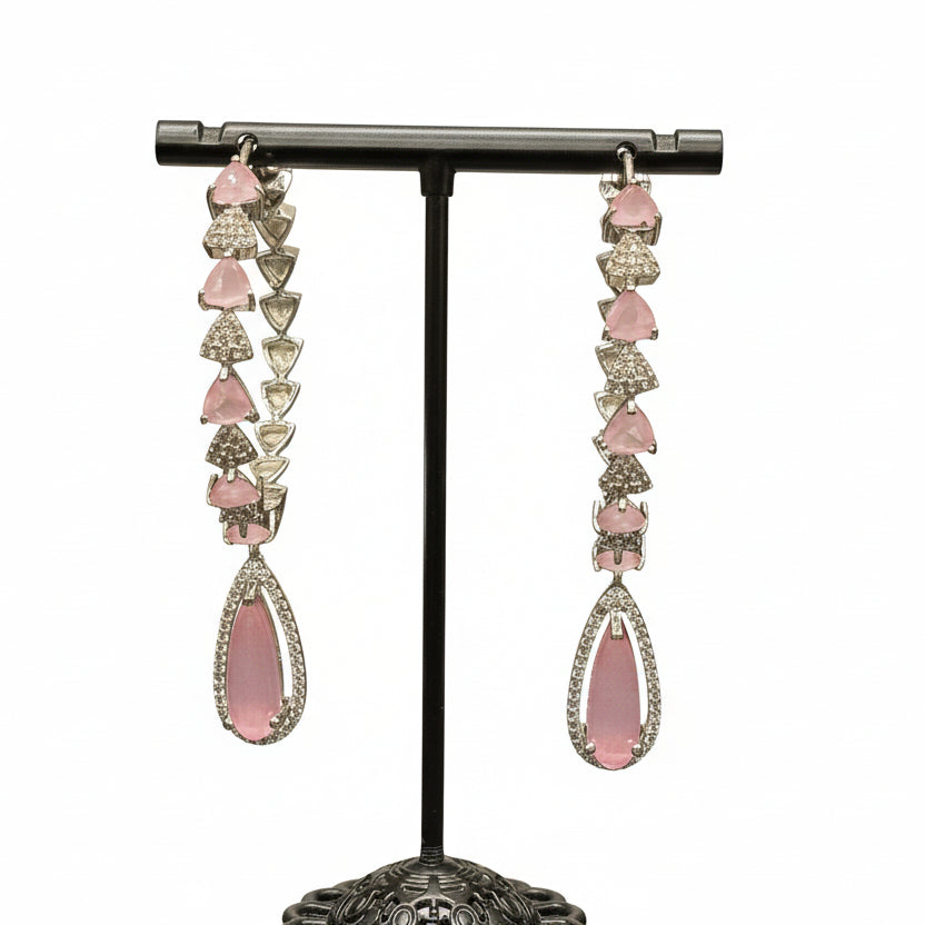 silver finish American diamond Jhumka bali earrings with green and clear stones on a stand.