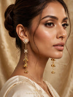 Model in a cream outfit wearing gold-tone Starlit Melody earrings with starburst tops and cascading ghungroo bells
