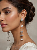 Model in a white outfit wearing silver-tone Starlit Melody earrings with starburst tops and long ghungroo bell drops.