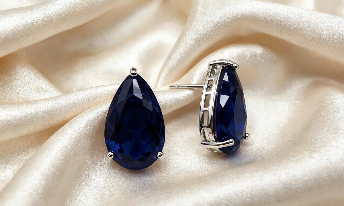 Navy blue teardrop crystal studs on cream fabric, showing the silver-tone setting and post from the side.