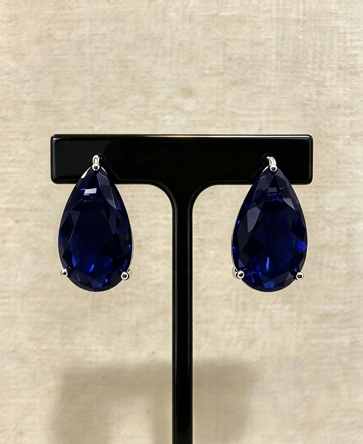 Navy blue teardrop crystal stud earrings in silver-tone three-prong settings on a black stand.