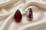 Ruby red teardrop crystal studs on cream fabric, showing the silver-tone setting and post from the side.