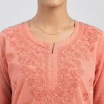 A close-up of a peach-pink embroidered kurta with a split neckline, shown on a mannequin torso with a delicate gold chain necklace.