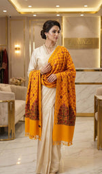 Woman wearing a white saree with a yellow shawl in an elegant interior setting